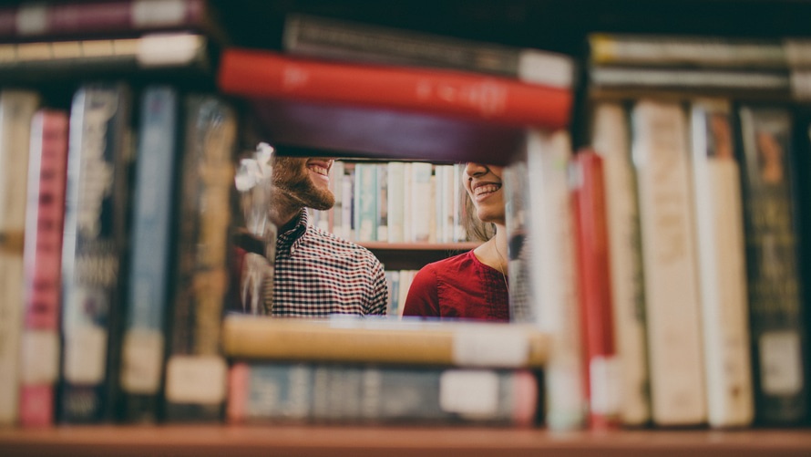 Man and woman smiling at one another surrounded by books.