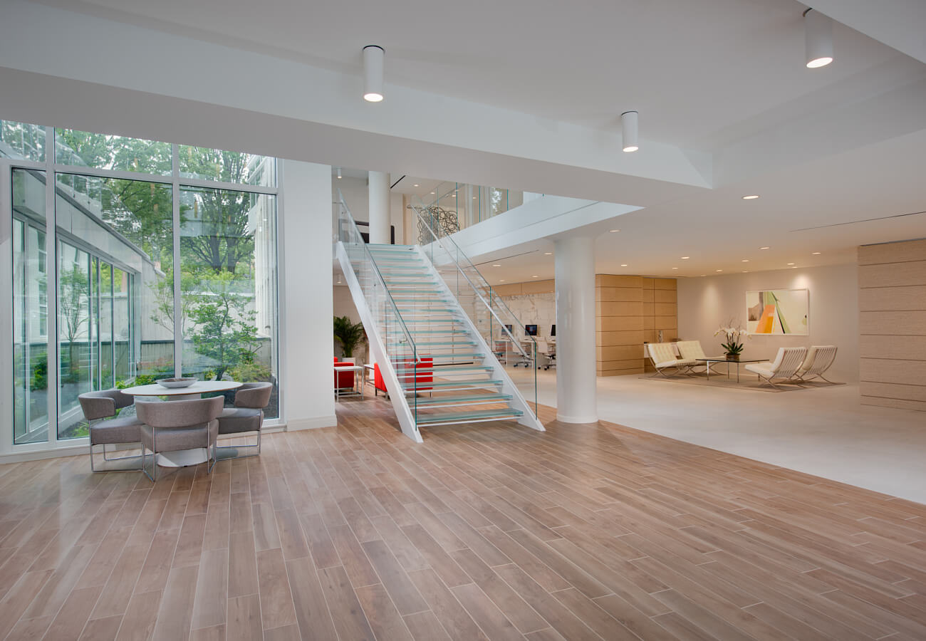 Downstairs lobby at Fifty Three Thirty Three Apartments with glass staircase, lounge seating, and large windows.