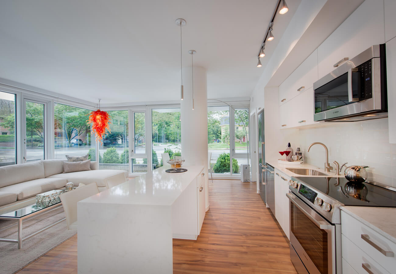 Model apartment kitchen at Fifty Three Thirty Three Apartments with white cabinetry, island, stainless appliances, and living area