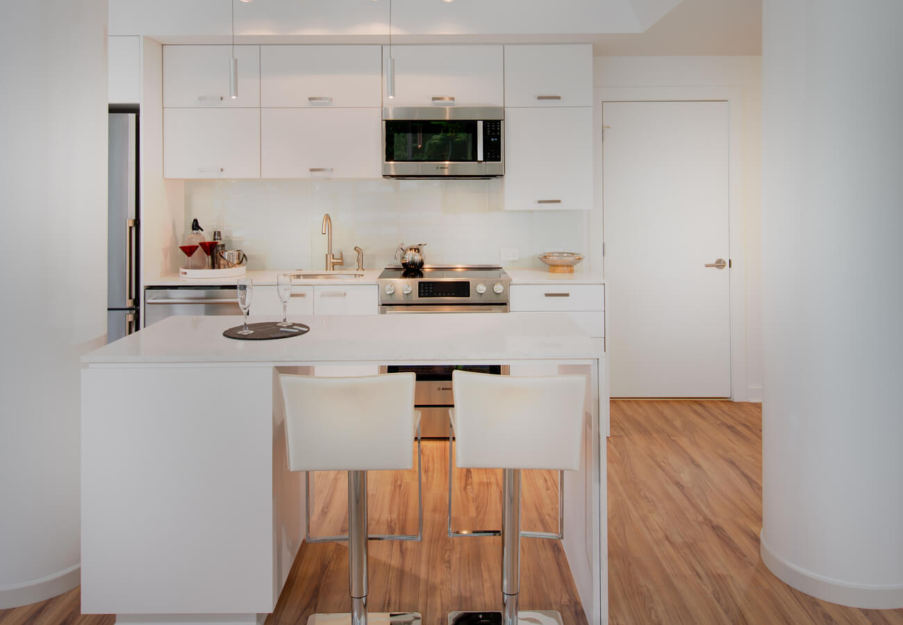 Model apartment kitchen at Fifty Three Thirty Three Apartments with white island, bar stools, pendant lights, and stainless appliances