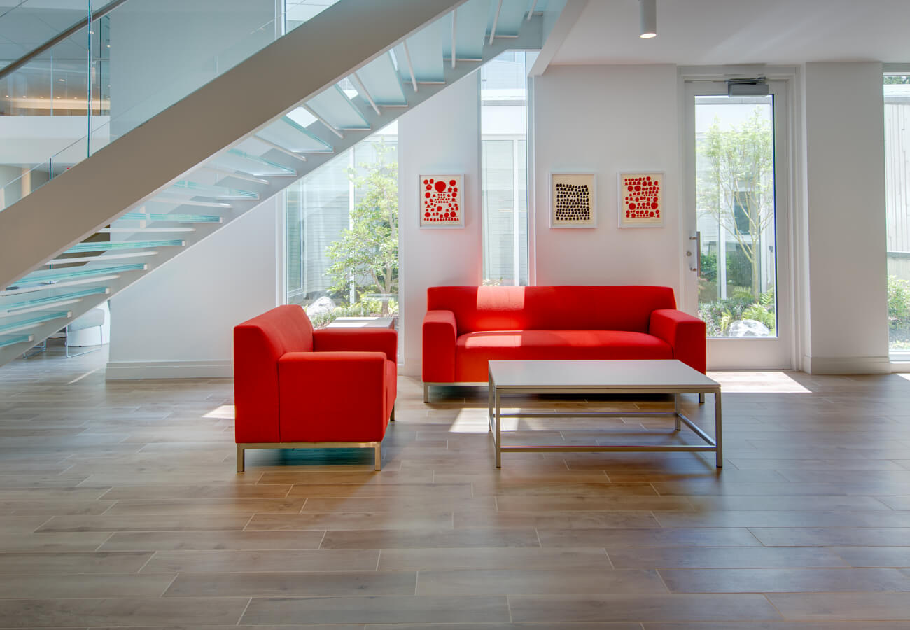 Downstairs lobby seating at Fifty Three Thirty Three Apartments with red sofa, glass staircase, and bright windows.