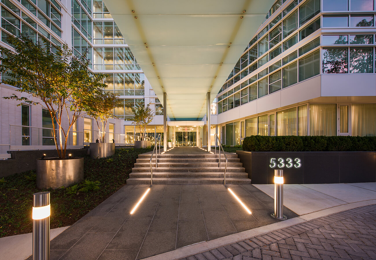 Nighttime entrance to Fifty Three Thirty Three Apartments with illuminated canopy, stairs, landscaping, and 5333 address sign.