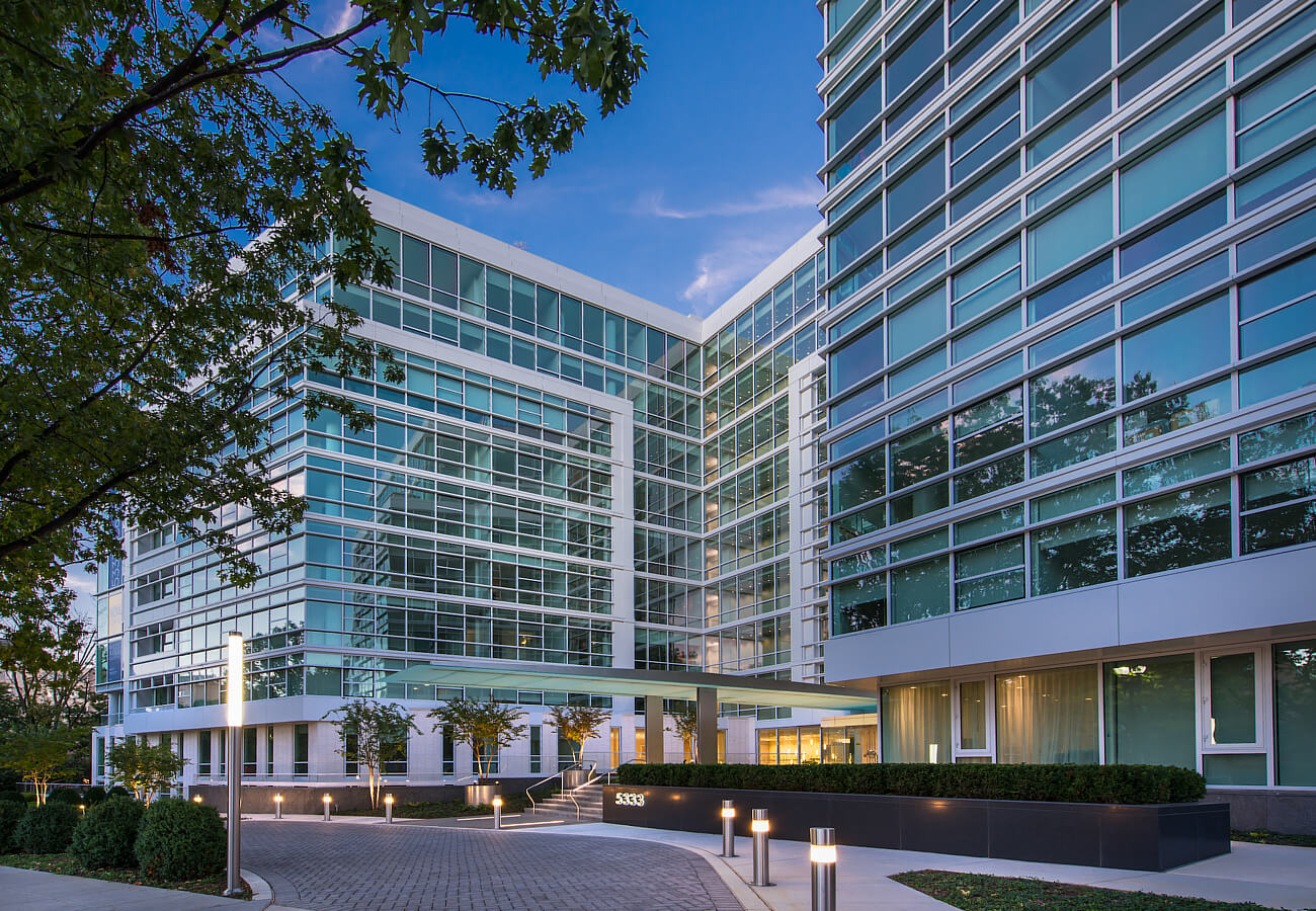 Evening exterior of Fifty Three Thirty Three Apartments with glass windows, landscaped entry, and illuminated walkway