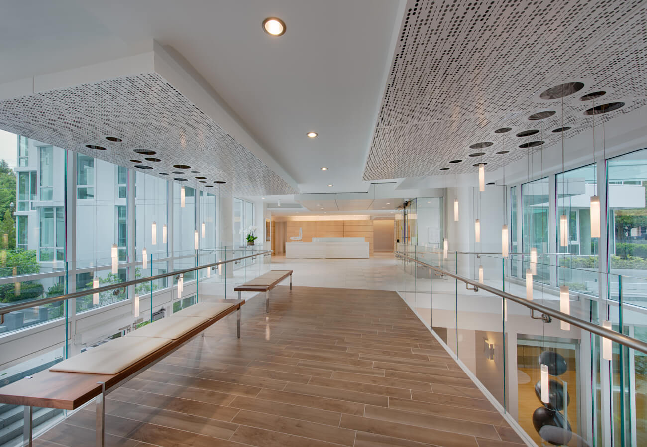 Upper lobby walkway at Fifty Three Thirty Three Apartments with glass railings, pendant lights, benches, and concierge desk.