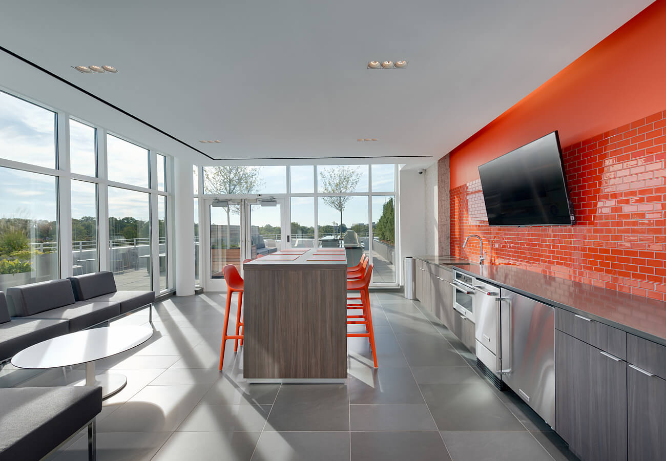 Rooftop lounge interior at Fifty Three Thirty Three Apartments with kitchen island, seating, TV, and terrace access.