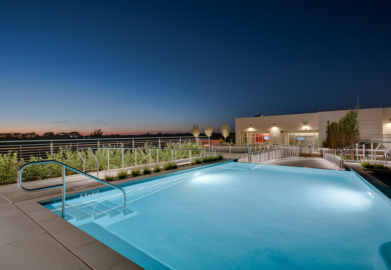 Nighttime rooftop pool at Fifty Three Thirty Three Apartments with glowing water, terrace lighting, and skyline views