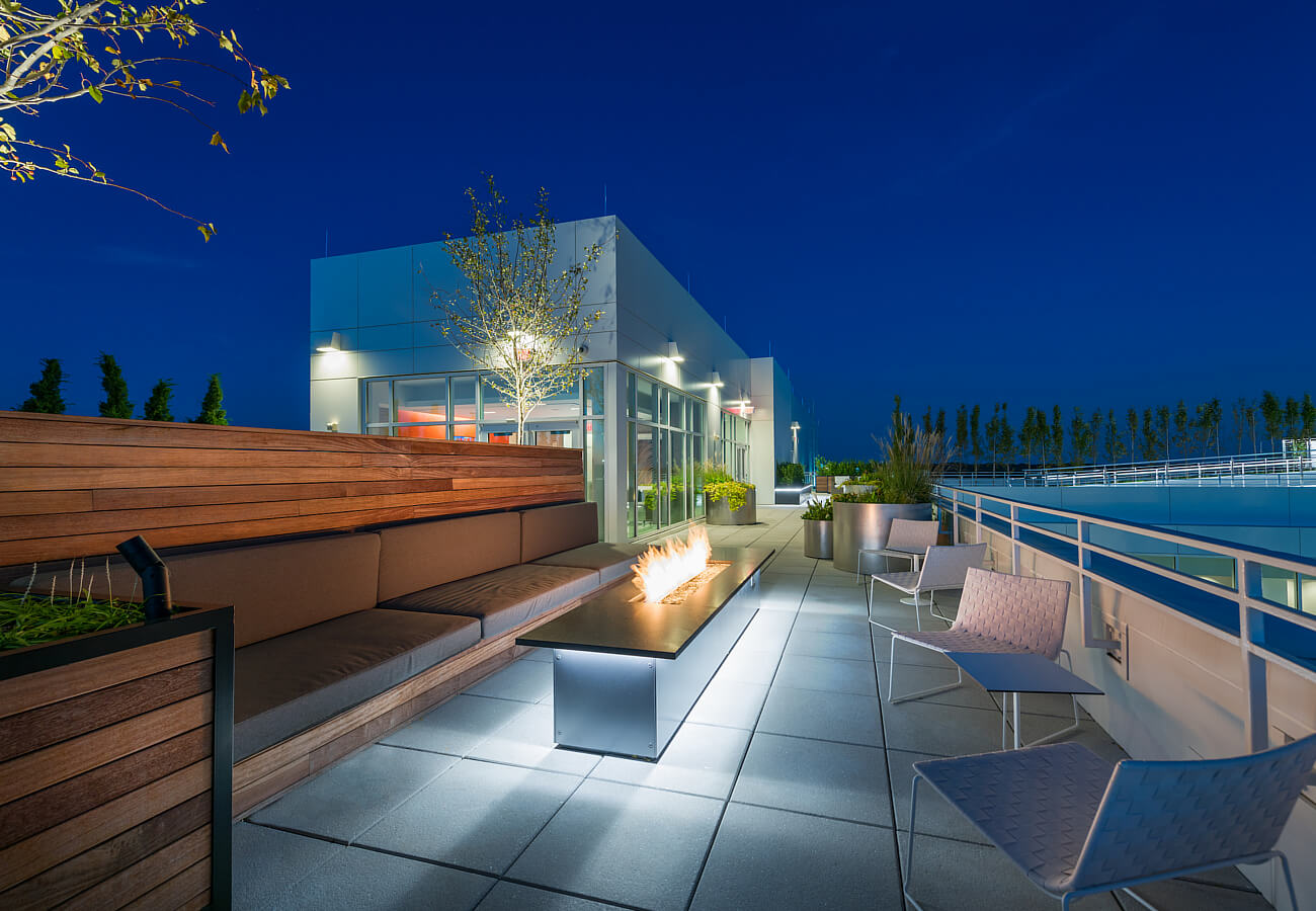 Nighttime rooftop terrace at Fifty Three Thirty Three Apartments with fire table, seating, and illuminated outdoor lounge